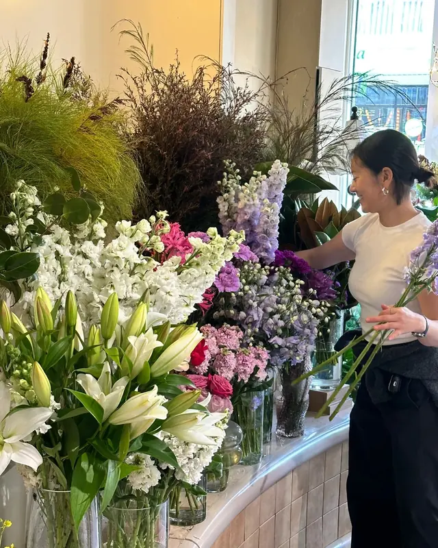 A Lamore florist choosing stems from buckets of lilies, stock, delphinium and roses in the shop