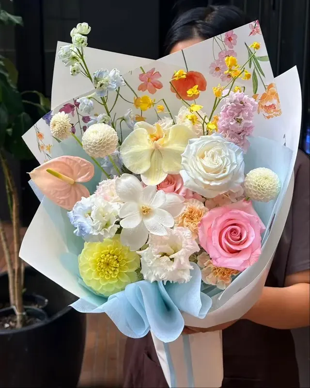 A pastel bouquet with a pink rose, white orchid, yellow dahlia and peach anthurium